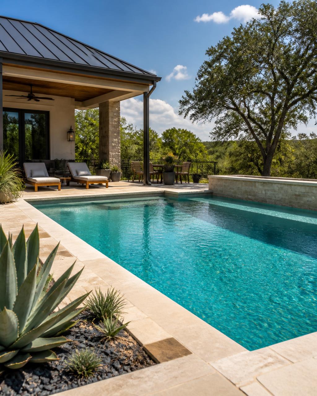 A bright turquoise swimming pool with limestone coping, agave landscaping and a covered patio overlooking Texas Hill Country trees.